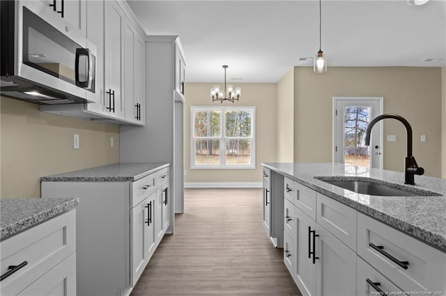 kitchen with sink, light hardwood / wood-style flooring, white cabinetry, hanging light fixtures, and light stone countertops