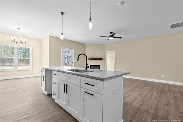 kitchen featuring sink, white cabinetry, light stone counters, decorative light fixtures, and an island with sink