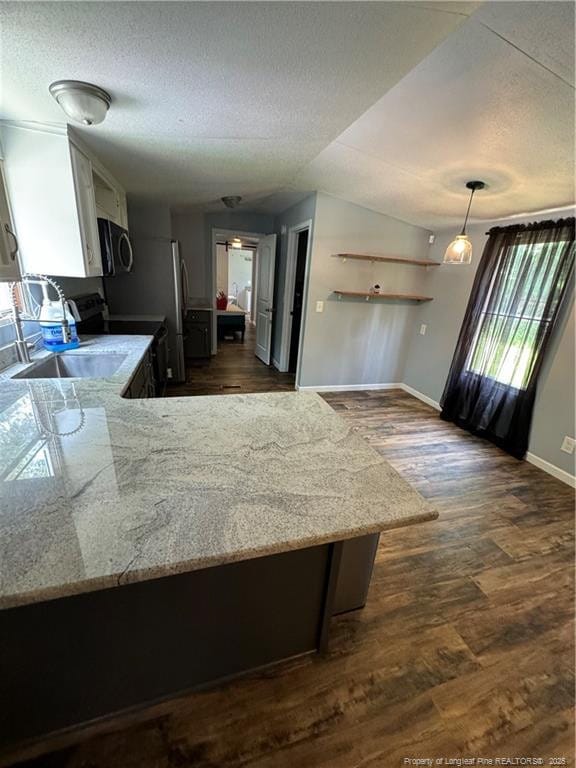 kitchen with appliances with stainless steel finishes, white cabinetry, dark hardwood / wood-style floors, decorative light fixtures, and kitchen peninsula