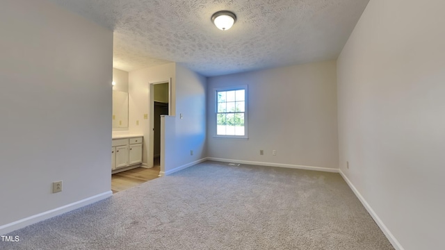 unfurnished bedroom featuring a textured ceiling, light carpet, and connected bathroom