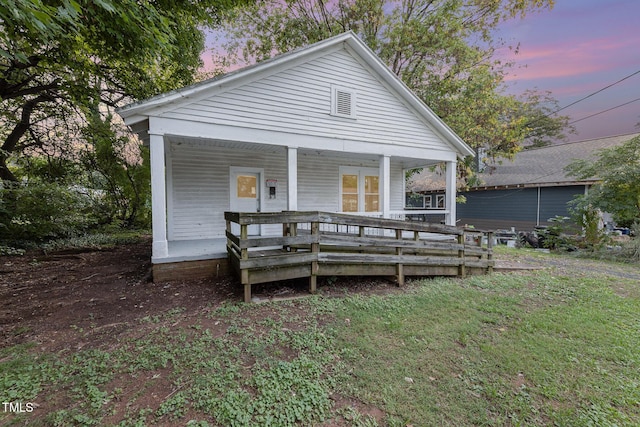 back house at dusk with covered porch and a lawn