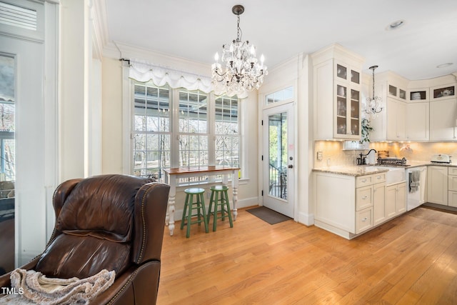 kitchen with an inviting chandelier, glass insert cabinets, backsplash, and light wood-style floors