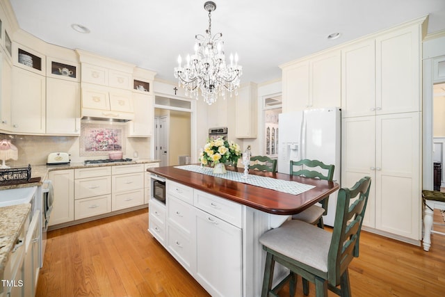 kitchen with light wood-style flooring, appliances with stainless steel finishes, a breakfast bar area, decorative light fixtures, and backsplash