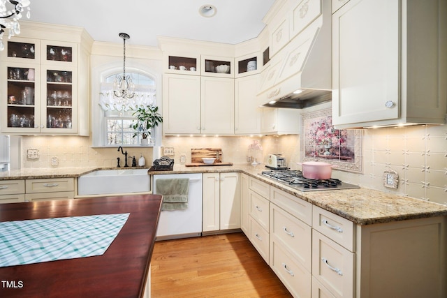 kitchen featuring light wood-style flooring, hanging light fixtures, premium range hood, stainless steel gas cooktop, and a sink