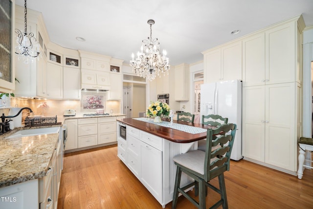 kitchen featuring white refrigerator with ice dispenser, a sink, a kitchen breakfast bar, light wood finished floors, and stainless steel gas stovetop