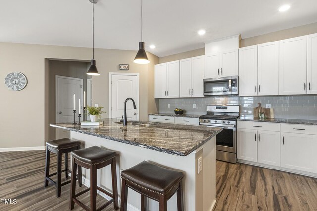 kitchen featuring dark wood finished floors, stainless steel appliances, backsplash, white cabinetry, and a sink