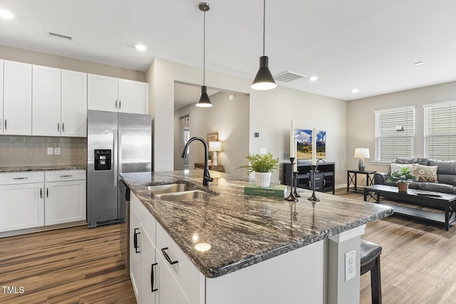 kitchen featuring a center island with sink, visible vents, wood finished floors, stainless steel refrigerator with ice dispenser, and a sink