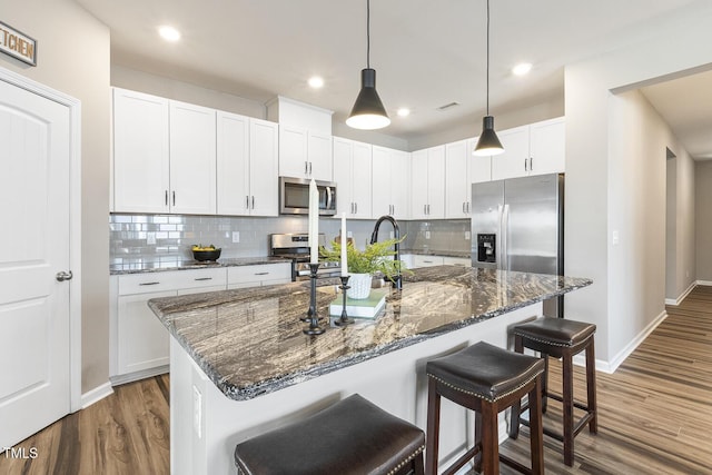 kitchen with white cabinets, dark stone counters, a breakfast bar, wood finished floors, and stainless steel appliances