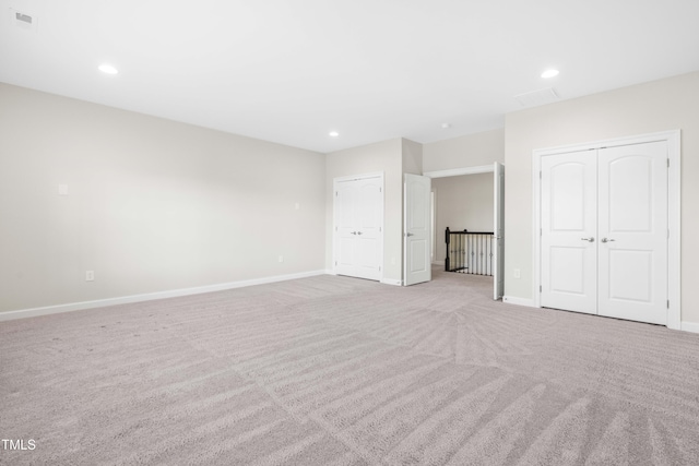 unfurnished bedroom featuring two closets, recessed lighting, light colored carpet, visible vents, and baseboards