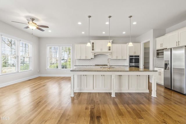 kitchen with dark stone countertops, white cabinets, stainless steel refrigerator with ice dispenser, and an island with sink