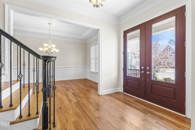 foyer featuring light wood finished floors, stairs, crown molding, french doors, and a notable chandelier