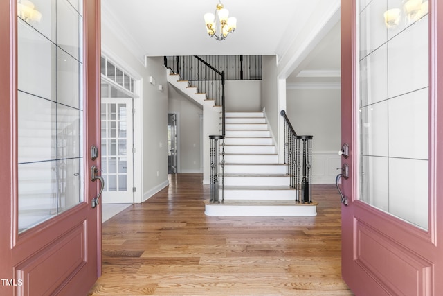 entrance foyer with light wood finished floors, stairway, an inviting chandelier, crown molding, and a decorative wall