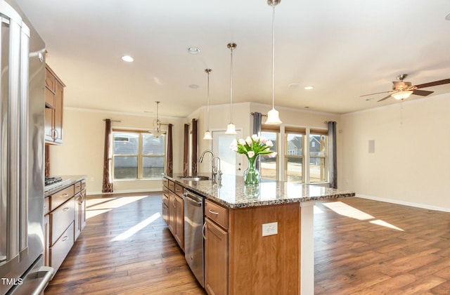 kitchen with dark wood-style flooring, a sink, appliances with stainless steel finishes, brown cabinets, and an island with sink