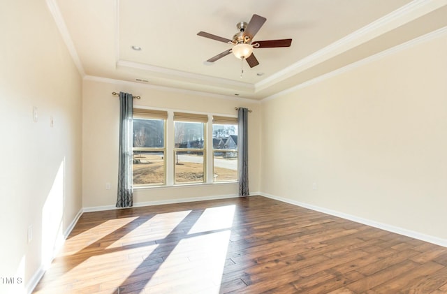 spare room featuring baseboards, wood-type flooring, ceiling fan, a tray ceiling, and crown molding