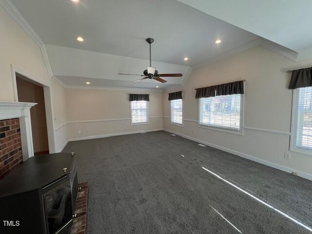 unfurnished living room with lofted ceiling, crown molding, a wood stove, dark carpet, and ceiling fan