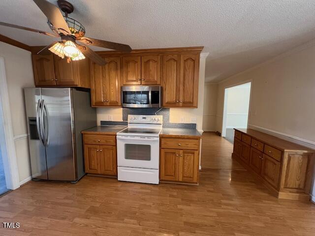 kitchen with ornamental molding, light hardwood / wood-style flooring, stainless steel appliances, and a textured ceiling