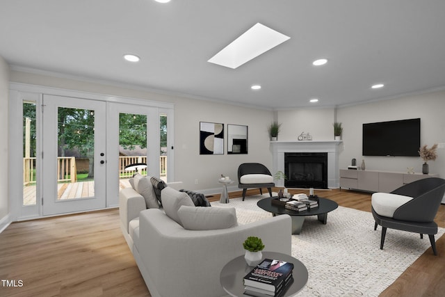 living room featuring recessed lighting, a fireplace, a skylight, ornamental molding, and light wood-type flooring