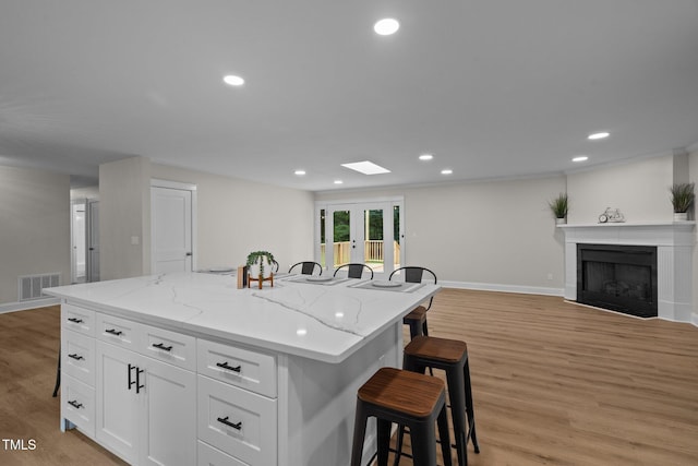 kitchen with visible vents, a kitchen island, french doors, a kitchen bar, and white cabinetry