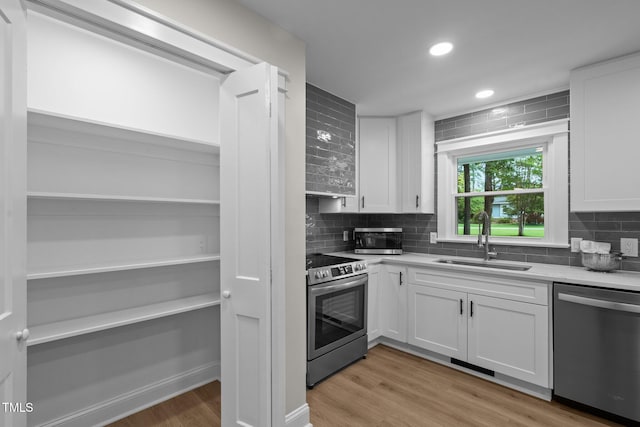 kitchen featuring stainless steel appliances, backsplash, a sink, and white cabinetry