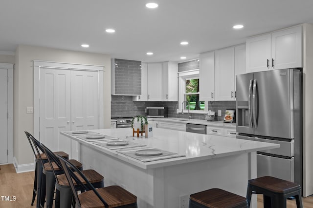 kitchen with light wood finished floors, white cabinets, appliances with stainless steel finishes, a kitchen bar, and backsplash