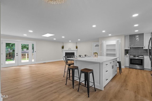 kitchen featuring a breakfast bar, stainless steel range with electric cooktop, light wood-type flooring, a fireplace, and backsplash