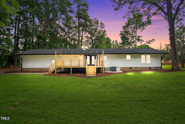 back of house at dusk featuring crawl space, a lawn, and a wooden deck