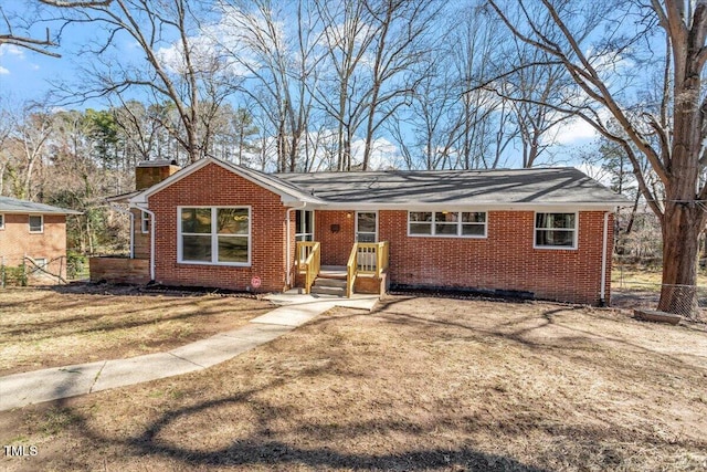 ranch-style house with a front yard, a chimney, fence, and brick siding