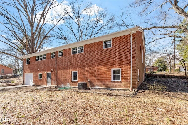 back of house with an attached garage, central air condition unit, and brick siding