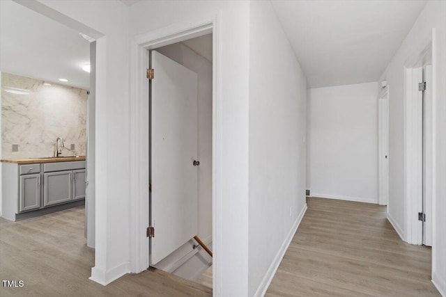 hall featuring an upstairs landing, a sink, light wood-style flooring, and baseboards