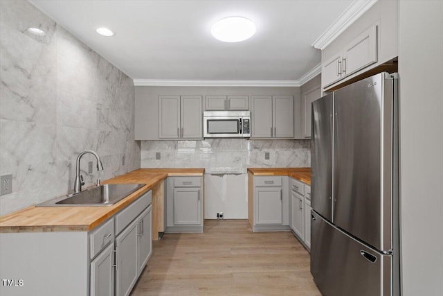 kitchen featuring light wood finished floors, stainless steel appliances, backsplash, ornamental molding, and a sink