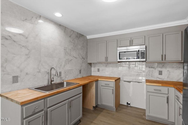 kitchen featuring tasteful backsplash, stainless steel microwave, wooden counters, gray cabinetry, and a sink