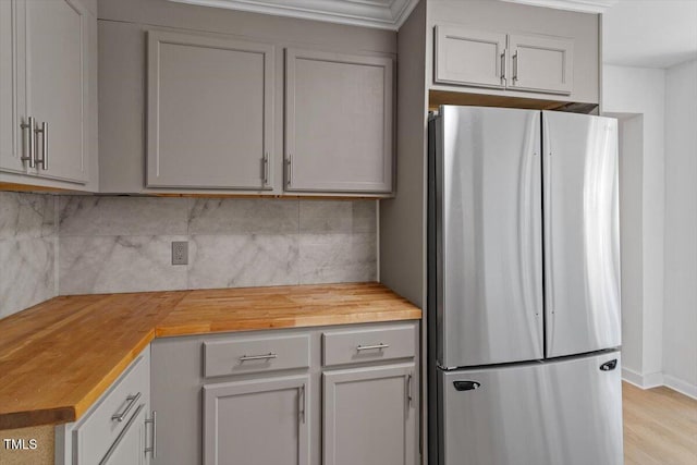 kitchen with wooden counters, decorative backsplash, light wood-style floors, freestanding refrigerator, and baseboards