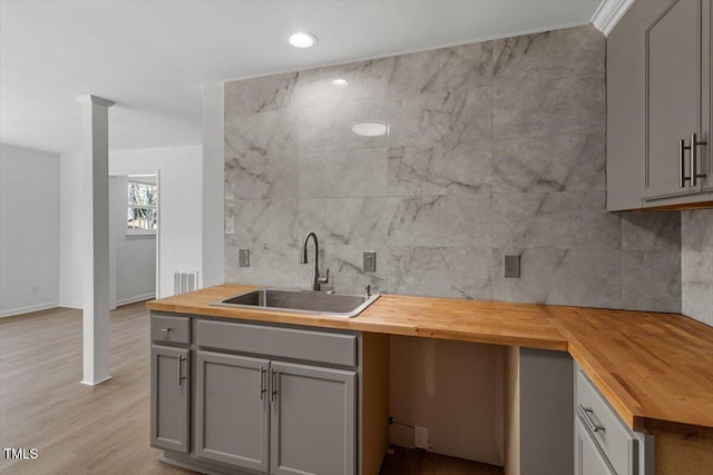 kitchen featuring gray cabinets, a sink, wood counters, and backsplash