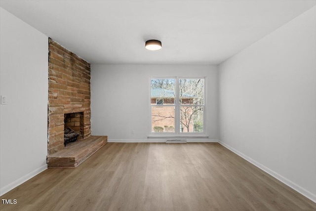 unfurnished living room with a brick fireplace, wood finished floors, and baseboards