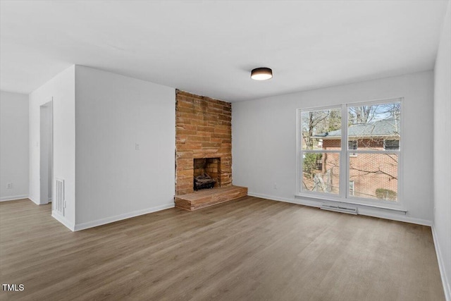 unfurnished living room with a large fireplace, visible vents, baseboards, and wood finished floors