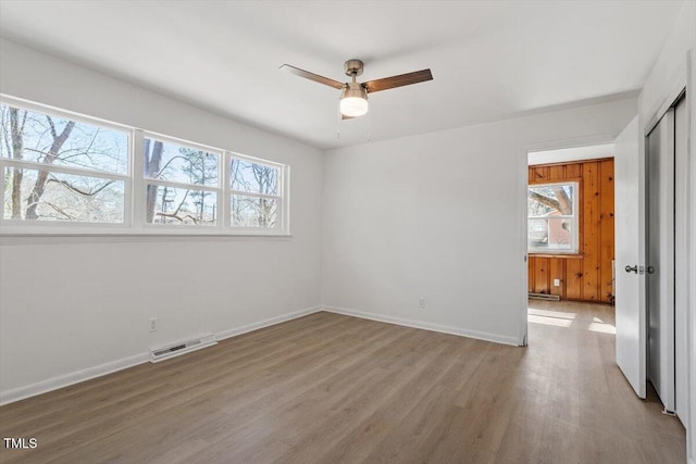 unfurnished bedroom featuring multiple windows, visible vents, baseboards, and wood finished floors