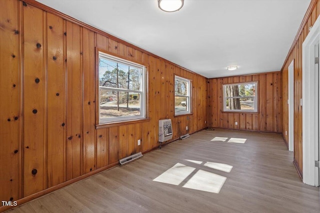 empty room featuring wooden walls, visible vents, baseboards, light wood-style flooring, and heating unit