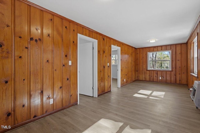 empty room featuring light wood-style flooring, wooden walls, baseboards, and an AC wall unit