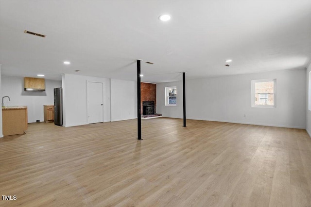 basement with light wood finished floors, visible vents, freestanding refrigerator, a brick fireplace, and a sink