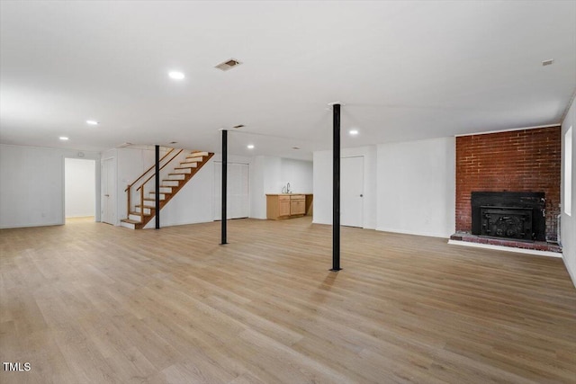 finished below grade area with visible vents, light wood-style flooring, stairs, a fireplace, and recessed lighting