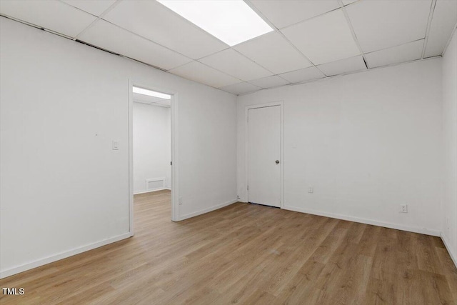 spare room featuring light wood-style flooring, baseboards, and a drop ceiling