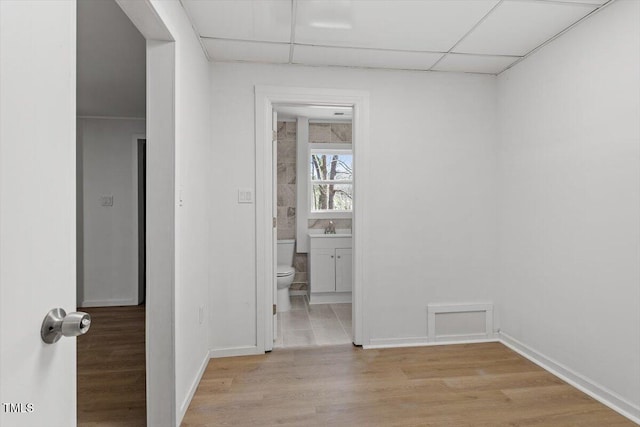 empty room featuring a drop ceiling, a sink, baseboards, and wood finished floors