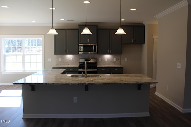 kitchen with appliances with stainless steel finishes, decorative light fixtures, an island with sink, ornamental molding, and light stone countertops