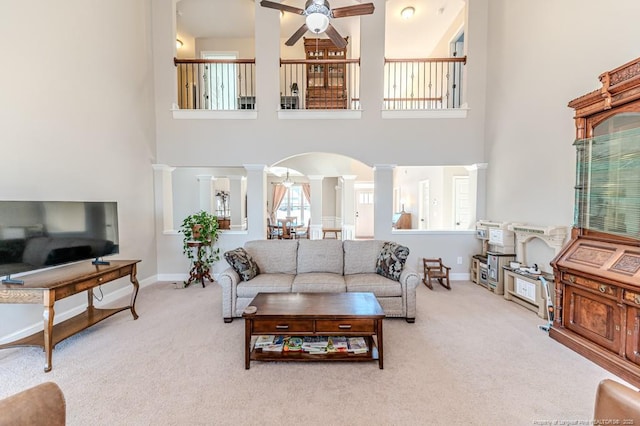 carpeted living room featuring decorative columns, ceiling fan, and a high ceiling