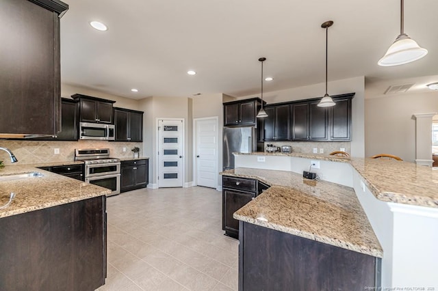 kitchen featuring sink, decorative light fixtures, light stone countertops, and appliances with stainless steel finishes