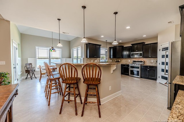 kitchen with light stone counters, pendant lighting, decorative backsplash, and appliances with stainless steel finishes