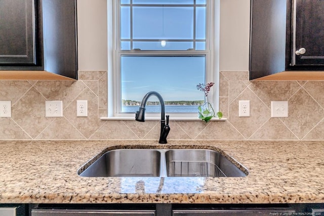 kitchen featuring light stone counters, sink, backsplash, and a water view