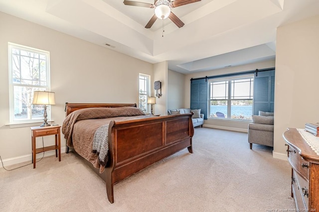 carpeted bedroom featuring a barn door, a water view, ceiling fan, and a tray ceiling