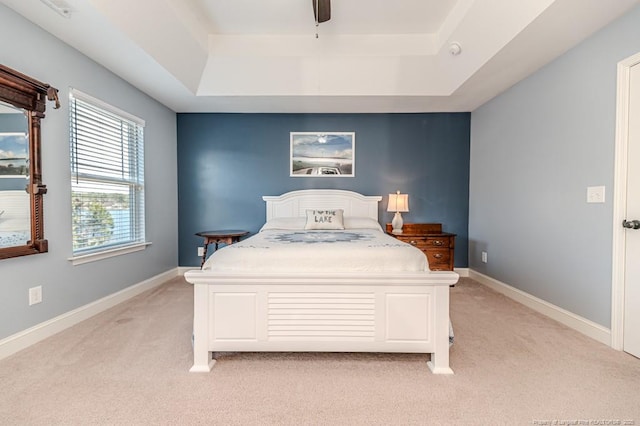 bedroom with a raised ceiling, light colored carpet, and ceiling fan