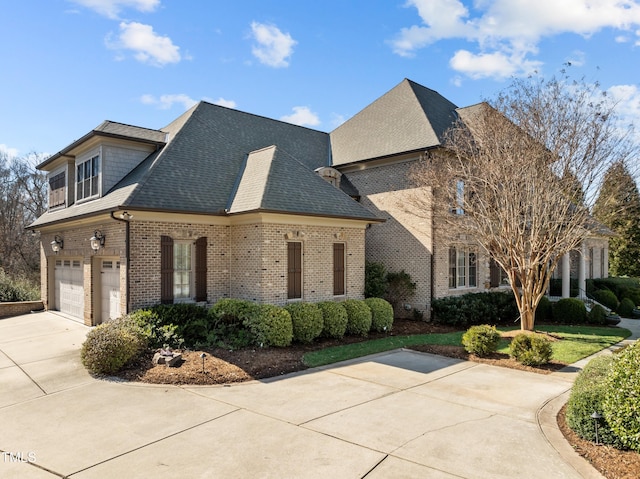 french country style house featuring a garage, concrete driveway, brick siding, and roof with shingles